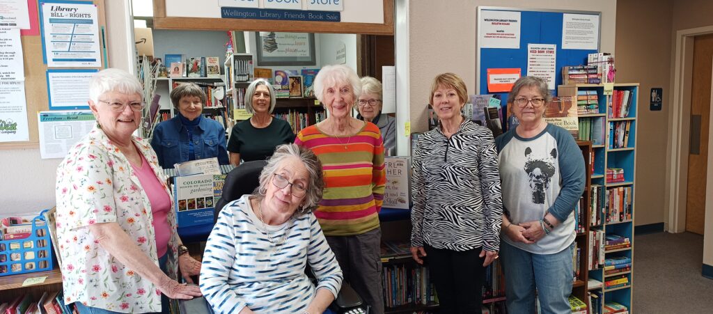 A photo of the Friends of the Wellington Public Library, a group of volunteers who support programs and services in the library, in front of the used bookstore that they run.